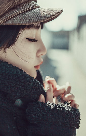Young woman in profile wearing hat and black coat with hands clasped