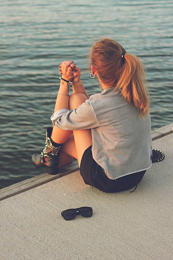 Woman sitting by water at sunset
