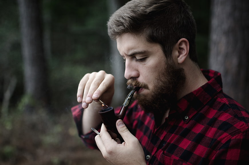 Bearded man lighting a pipe in the forest