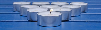 Single lit tealight candle among unlit ones on blue wood