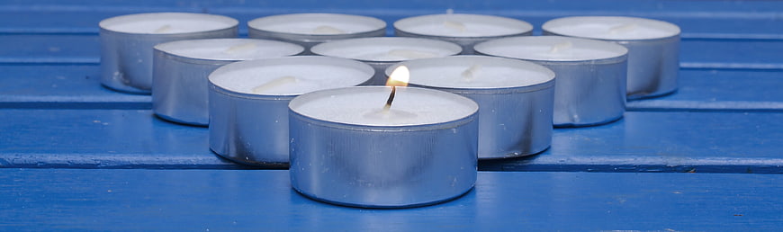 Single lit tealight candle among unlit ones on blue wood