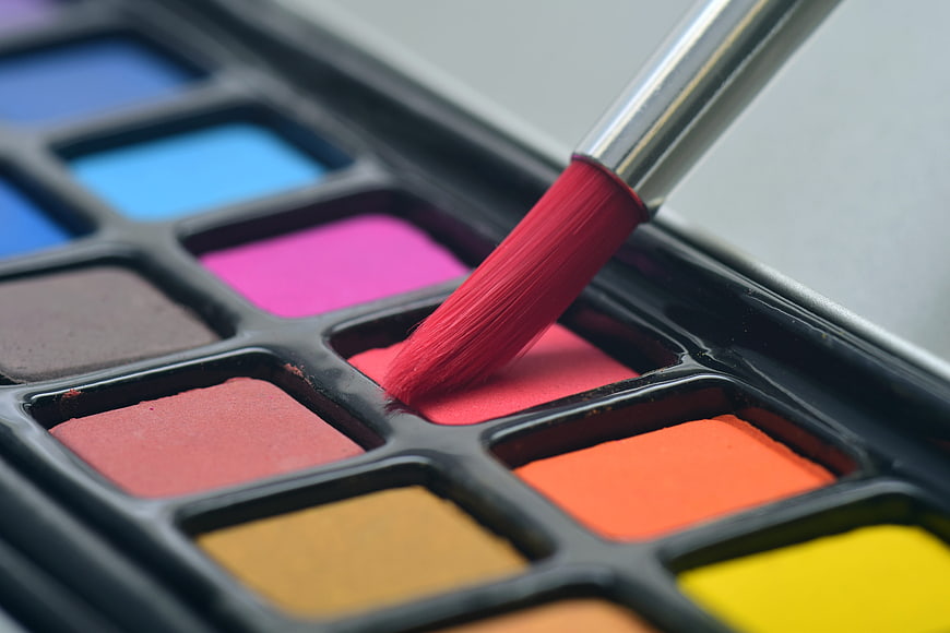 Close-up of paintbrush dipping into red watercolor palette