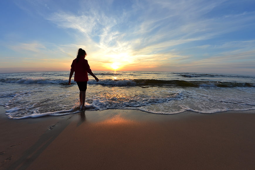 Woman Walking on Beach at Sunset with Ocean Waves