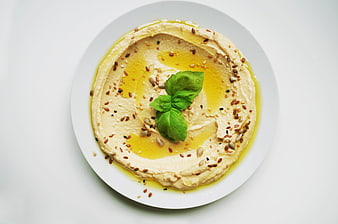 Hummus with olive oil, seeds, and fresh basil on a white plate