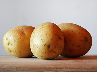 Three raw yellow potatoes on a wooden board