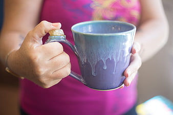 Hands holding handmade blue ceramic mug with dripping glaze