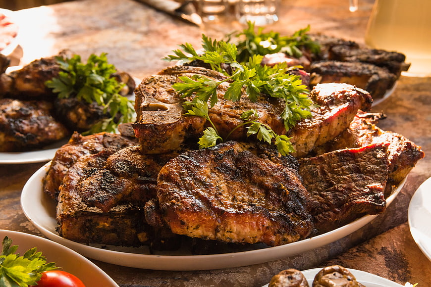 Platter of grilled steaks with parsley garnish on rustic table