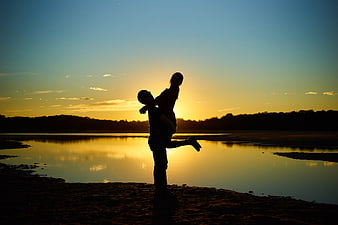 Silhouette of a couple hugging by a lake at sunset