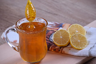 Glass mug of golden honey with honey dipper and fresh lemon halves on wooden table