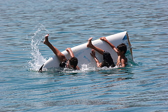 Three boys playing with a surfboard in the ocean