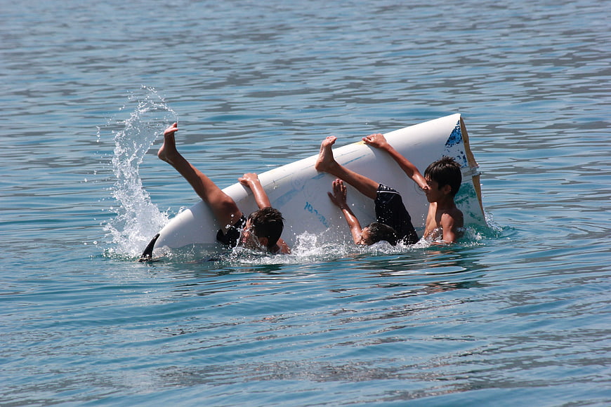Three boys playing with a surfboard in the ocean
