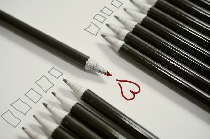 Red pencil drawing heart among black pencils on checklist