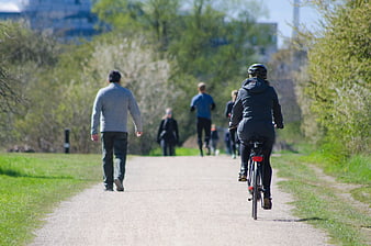 People walking and cycling on a gravel path in a sunny urban park