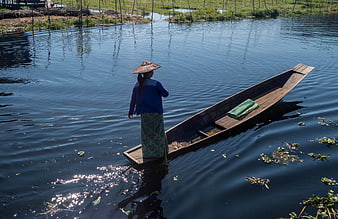 Woman in conical hat paddling wooden boat on river