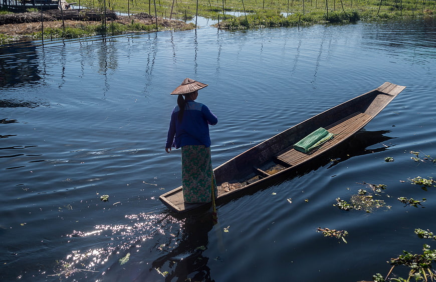 Woman in conical hat paddling wooden boat on river