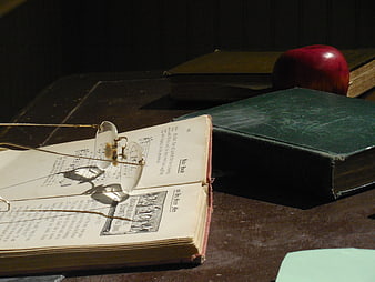 Vintage open book with reading glasses and apple on wooden desk