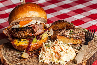 Gourmet burger with fried egg, bacon, and potato wedges on wooden board