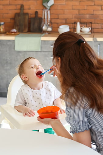Mother Feeding Happy Toddler in High Chair