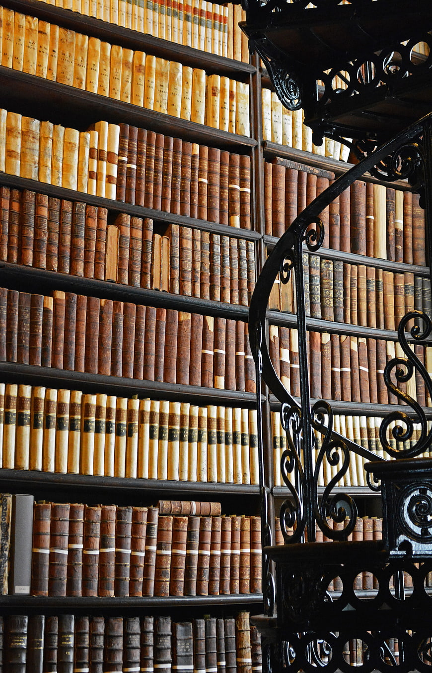 Vintage leather-bound books on shelves with ornate black iron spiral staircase