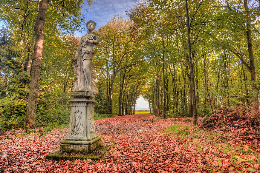 Classical Statue in Autumn Forest Path with Red Leaves