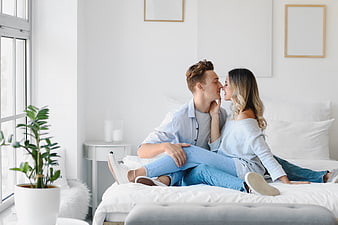 Happy couple sitting on bed in bright bedroom