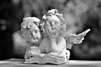 Black and white photo of two cherub statues reading a book