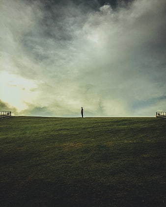 Solitary man standing on grassy hill under dramatic cloudy sky