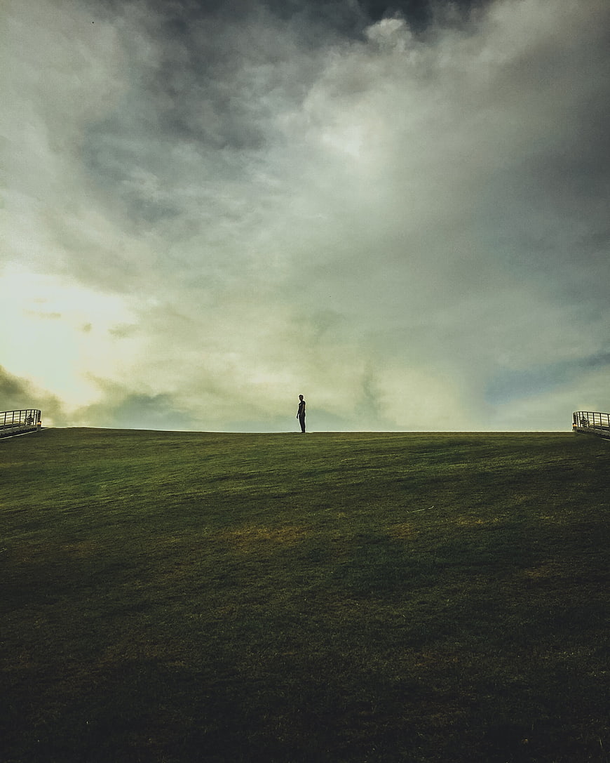 Solitary man standing on grassy hill under dramatic cloudy sky