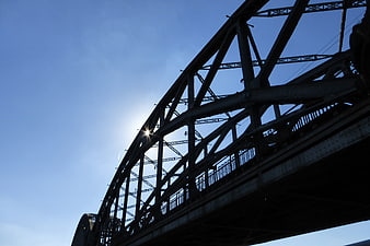 Silhouette of steel truss bridge against blue sky