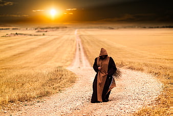 Hooded Monk Walking on Gravel Path at Sunset