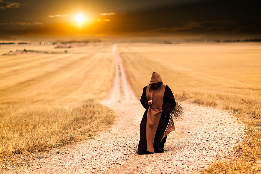 Hooded Monk Walking on Gravel Path at Sunset