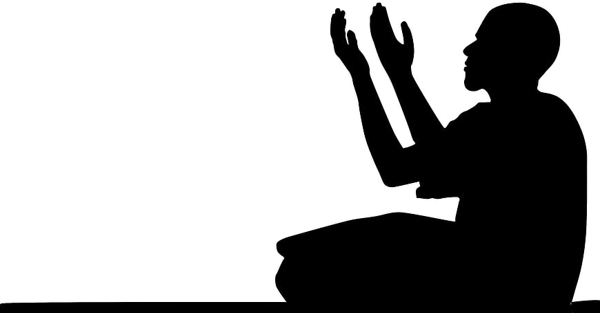 Silhouette of man praying with hands raised