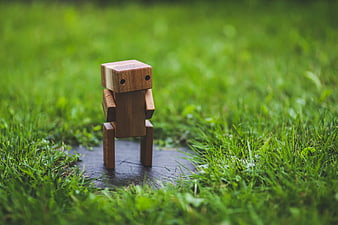 Small wooden robot toy standing on wet stone in green grass