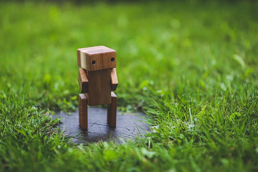 Small wooden robot toy standing on wet stone in green grass