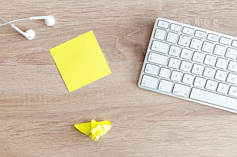 Flat lay of white keyboard, yellow sticky note, and earphones on wooden desk