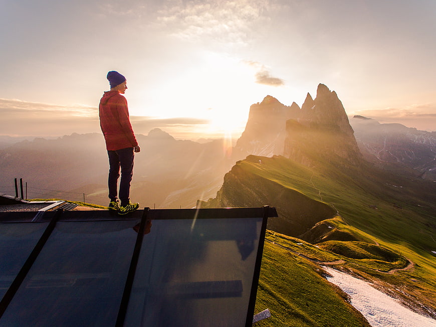 Hiker Standing on Glass Platform Overlooking Mountain Sunset