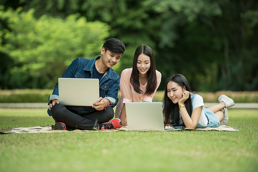 Young Asian Students Studying Together on Laptops in Park