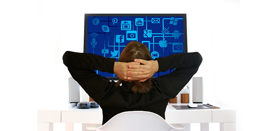 Woman relaxing at desk with social media icons on monitor