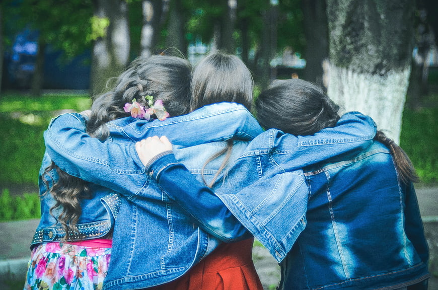 Three female friends hugging in denim jackets outdoors