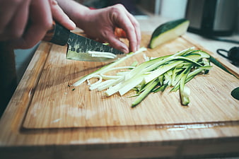 Hands slicing zucchini on wooden cutting board