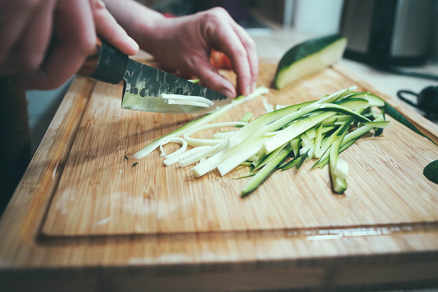 Hands slicing zucchini on wooden cutting board