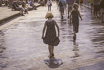 Two young girls walking away on wet brick pavement