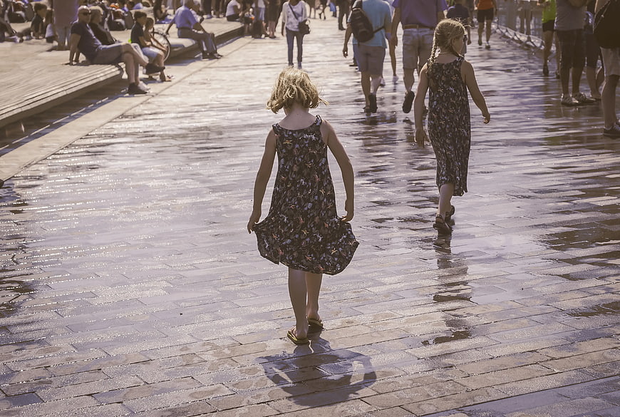 Two young girls walking away on wet brick pavement