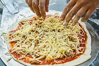 Hands Sprinkling Shredded Cheese On Raw Pizza With Tomato Sauce