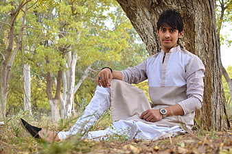 Young man in traditional kurta sitting under tree outdoors