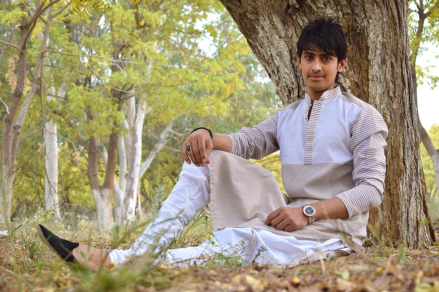 Young man in traditional kurta sitting under tree outdoors