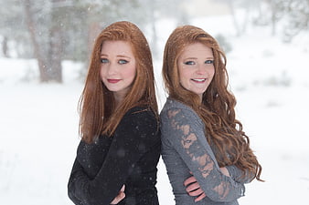 Two Redheaded Sisters Standing Back to Back in Snowy Winter Landscape