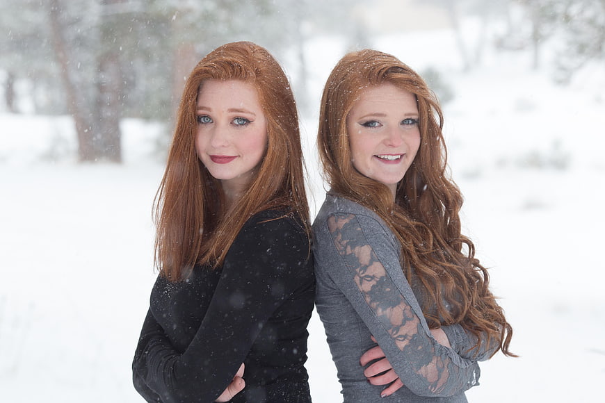Two Redheaded Sisters Standing Back to Back in Snowy Winter Landscape