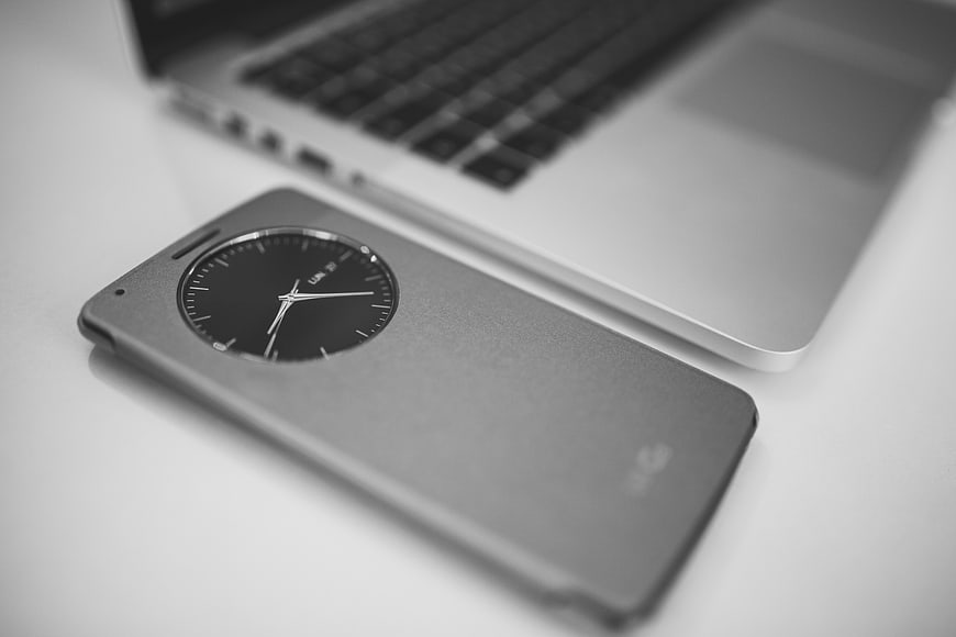 Black and white smartphone with analog clock display on desk