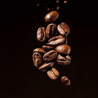 Roasted coffee beans falling against dark background